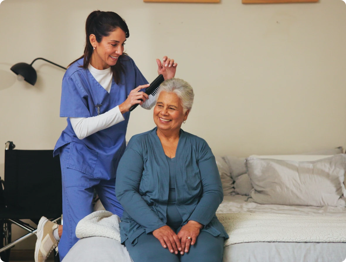 Caregiver combing elderly woman's hair, both smiling.