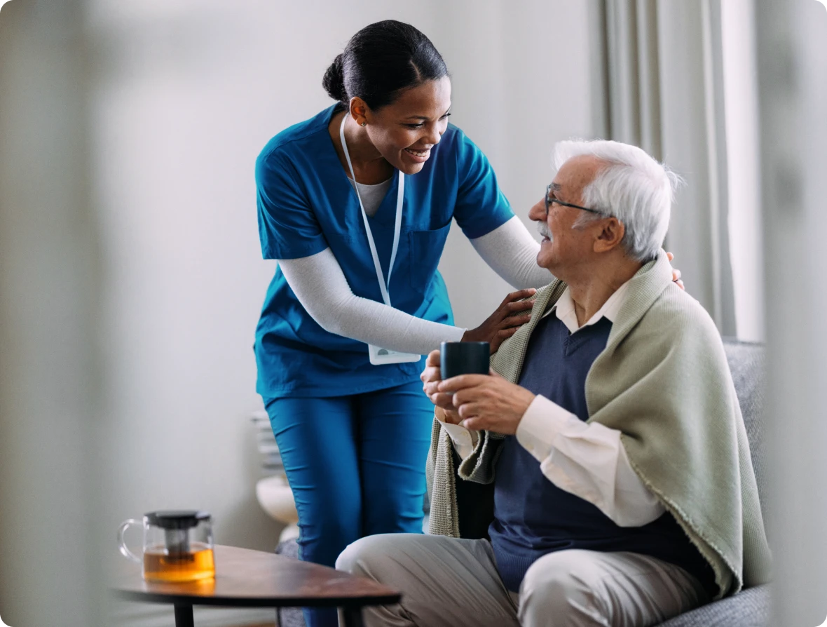 Nurse assisting elderly man with drink.