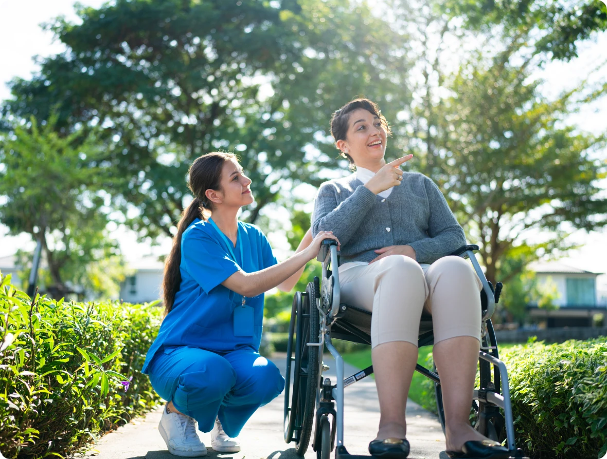 Person in wheelchair outside with caregiver talking.
